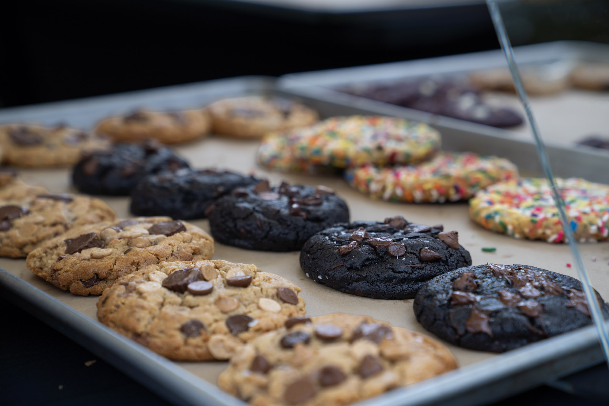 Our real chocolate chunk, double chocolate and confetti cookies lined up on a tray